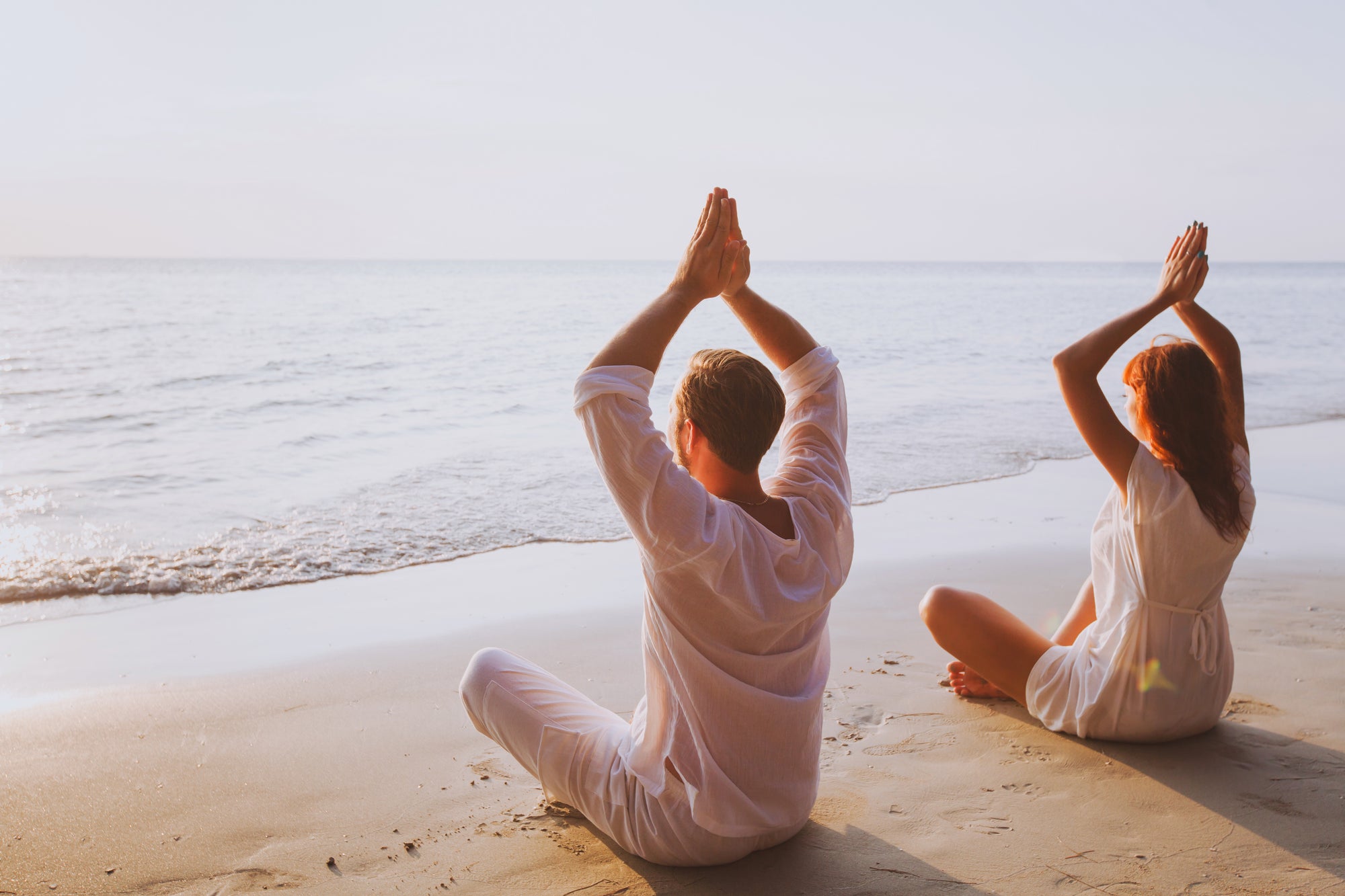 Couple on the beach doing yoga 