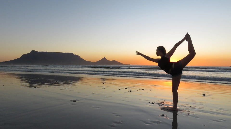 Young woman doing najarasana dancer pose on a beach