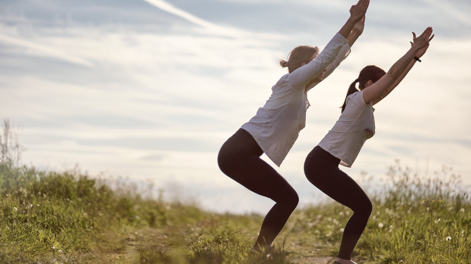 Two ladies in a park practicing the yoga posture utkatasana - the chair or fierce pose