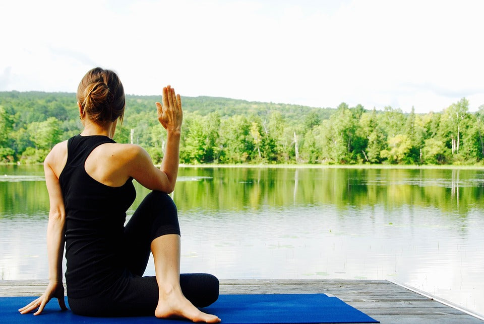Lady performing seated spinal twist yoga pose beside a lake